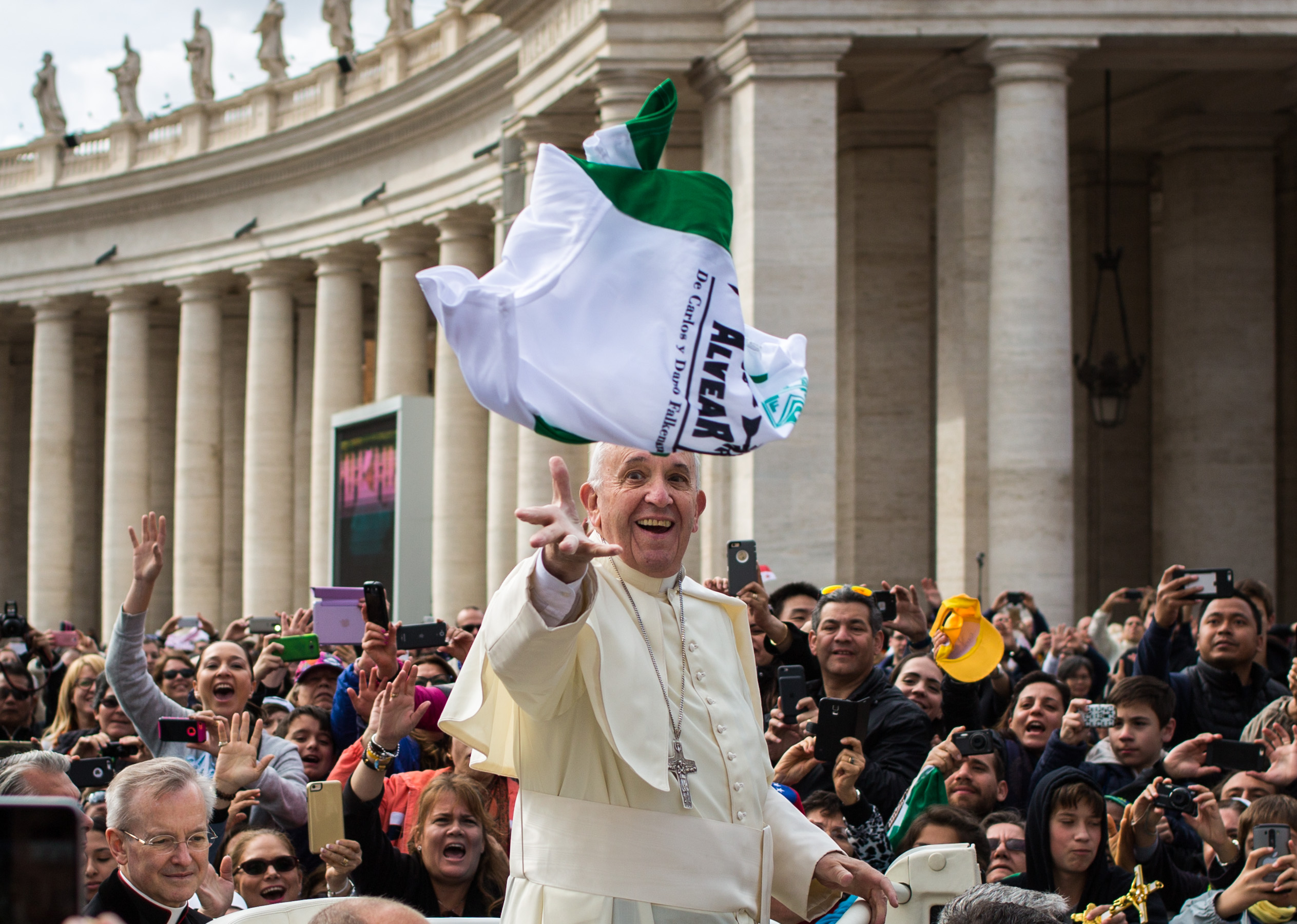 Pope Francis reaches to catch a flag that is thrown to him from a crowd