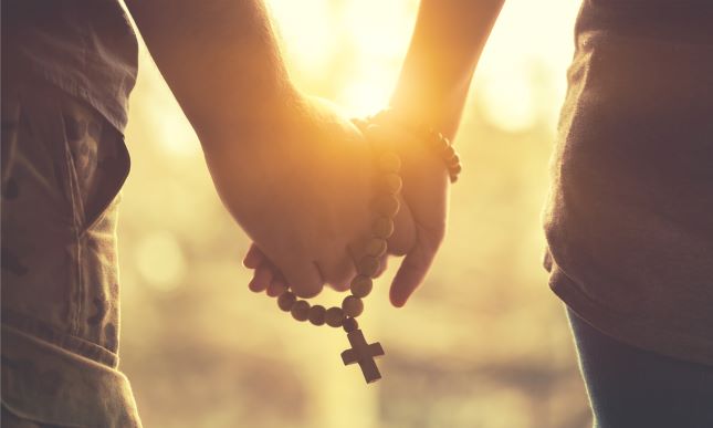 couple holding hands and a rosary walking way from viewer during sunset